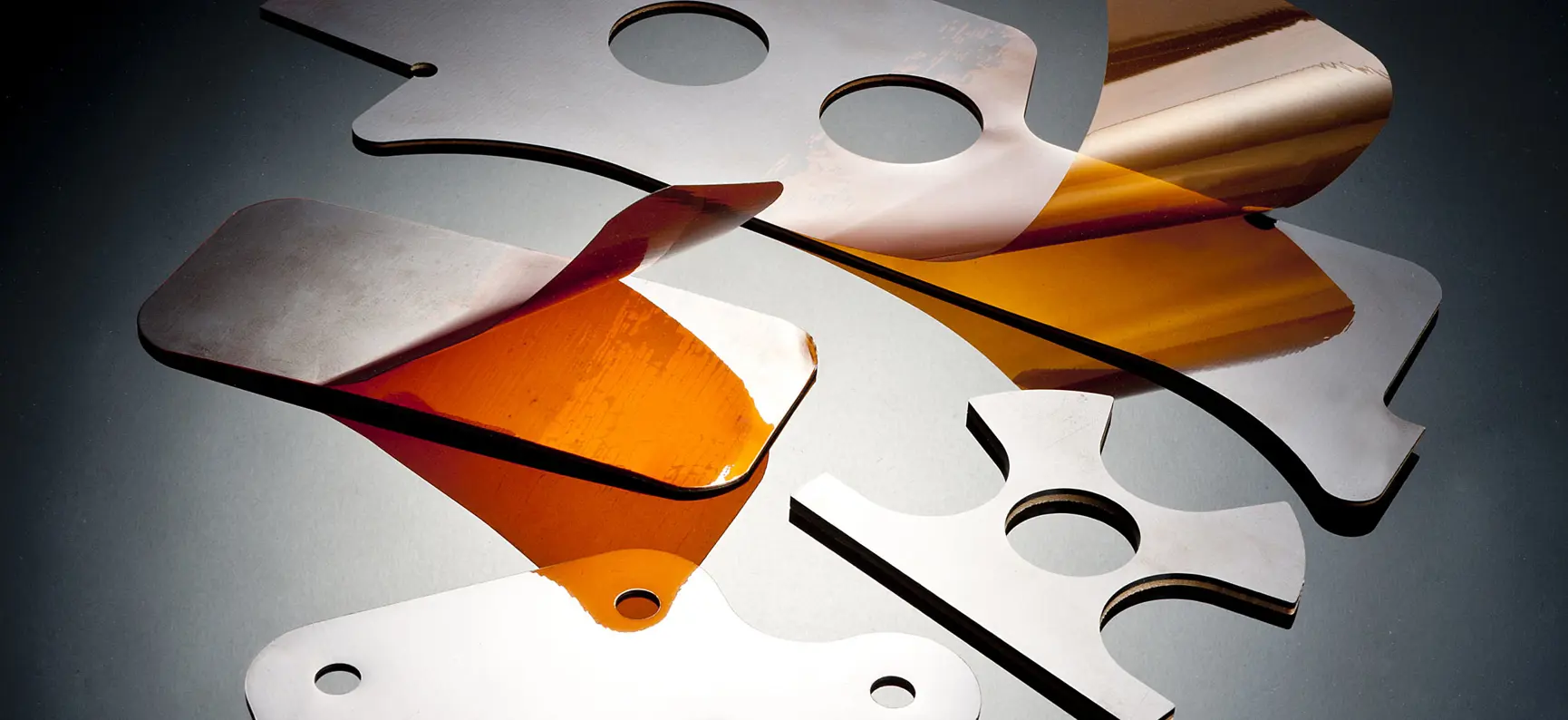 Precision-machined aerospace shims in metallic and amber materials, showing a range of custom shapes and sizes manufactured by Avantus Aerospace.